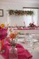 Dekoracja weselna w Dworku Piotrków – kolorowa aranżacja sali z kwiatami i girlandą Dekoracja weselna w Dworku Piotrków – długie stoły z białymi obrusami, różowymi materiałami, świecami oraz girlandą kwiatową zawieszoną nad stołem