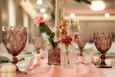 Różowa dekoracja stołu weselnego z elegancką zastawą Elegancki stół weselny z różowymi kieliszkami, pastelową dekoracją i złotymi świecznikami.